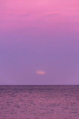 Large glowing full moon rising over the dark horizon of the Mediterranean Sea in Malta, partially covered by soft horizontal clouds during twilight.