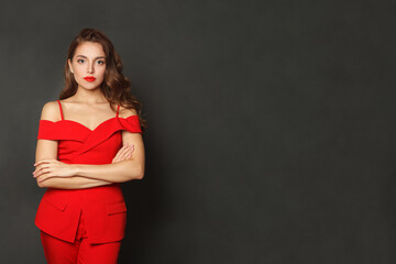 Glorious young woman in red suit standing against black studio wall background