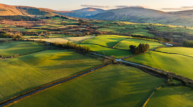 Aerial view of patchwork fields glow in the golden light, contrasting with the shadows cast by the rolling hills, Brecon, Wales, United Kingdom.