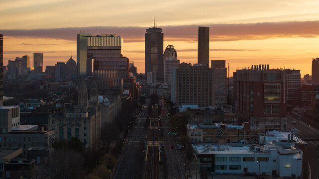 Aerial view of buildings casting long shadows as the sun sets behind Prudential Tower and the John Hancock Tower, Boston, Massachusetts, United States.
