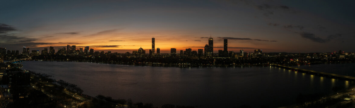 Aerial view of the Charles River reflecting the city lights under a fiery sunset, showcasing iconic skyscrapers like the Prudential Center, Boston, Massachusetts, United States.