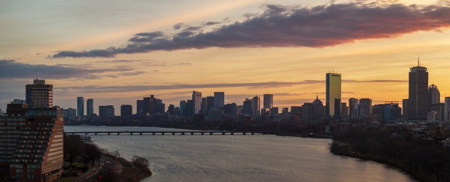 Aerial view of a tranquil river reflecting the warm hues of the sunset sky, framed by the iconic skyline and bridge, Boston, Massachusetts, United States.