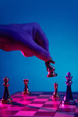 Hand holding chess knight above game board in neon. Concept of unconventional move, surprise tactic, probability play, gambling behavior, creative business thinking, strategic disruption.