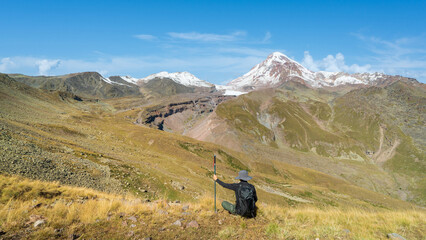 Man sitting on mountain slope resting and enjoying breathtaking snow-covered peaks and vast scenery.