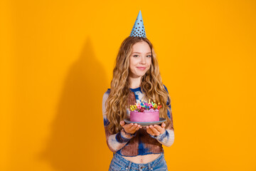Young stylish woman celebrates birthday with a colorful cake and candles wearing a party hat against a bright yellow background expressing joy celebration and festive vibe