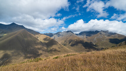 Obraz premium Scenic highland valley in Georgia with dramatic Caucasus mountains under blue sky and clouds.