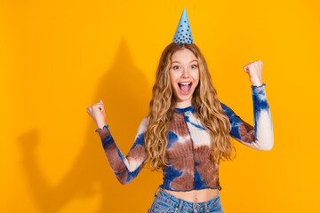 Young woman celebrates birthday with party hat and tie dye top against yellow background