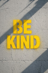 Yellow Be Kind Graffiti Stencil On Gray Cracked Concrete Wall With Shadows