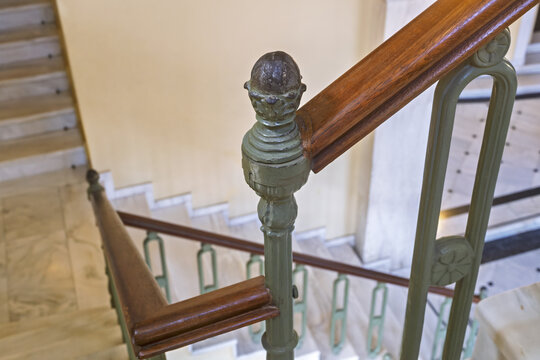 Interior view of the Apollon Theater in Ermoupolis, Syros, Greece, showing a descending staircase with green-painted balusters and dark wooden handrails.