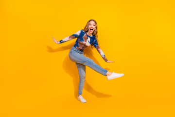 Young woman in tie dye top and jeans jumps with joy against a bright yellow background in a casual fashion shoot