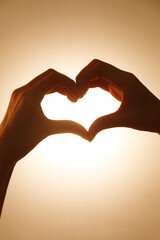 Fototapeta premium Heart Hand Gesture Silhouette Against Golden Sky