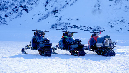 Three snowmobiles parked in a snowy mountain landscape, representing winter sports, adventure tourism, and outdoor winter activities