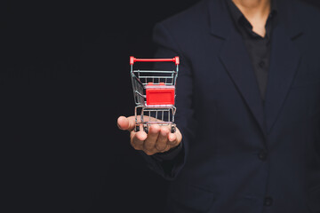 Businessman holding mini shopping cart on dark background.