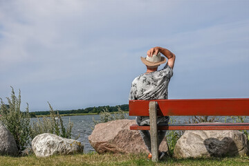 Mann sitzt mit Hut auf der Holzbank an der Ostsee