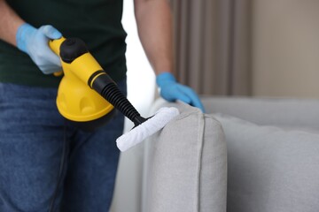 Pest control worker cleaning sofa with steam cleaner indoors, closeup