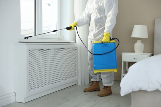 Pest control worker in protective suit spraying insecticide indoors, closeup