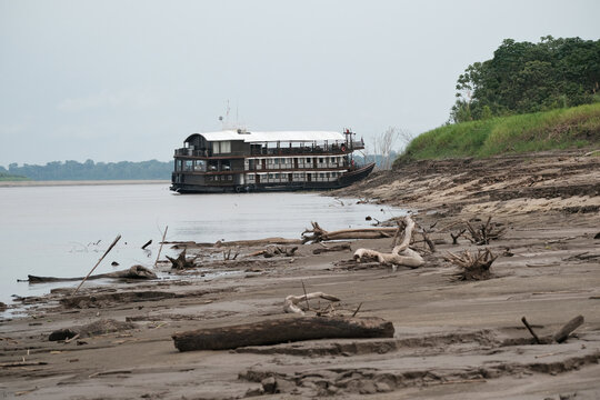 Large riverboat resting on the muddy riverbank of the ucayali river, amidst driftwood and jungle vegetation under a cloudy sky