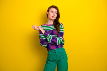 Young woman in striped sweater and green pants stands against a bright yellow background