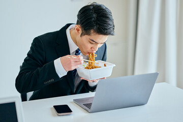 カップ焼きそばを食べながら仕事をする20代の若い男性