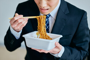 カップ焼きそばを食べながら仕事をする20代の若い男性