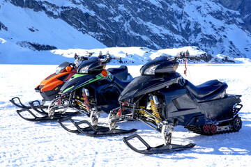 Three colorful snowmobiles parked on a snowy landscape, showcasing vibrant designs and sleek...