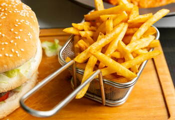 Delicious burger and fries on a wooden serving board with a metal basket of fries beside it