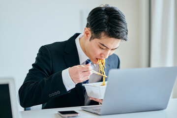 カップ焼きそばを食べながら仕事をする20代の若い男性