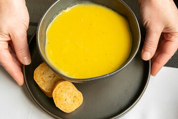 Warm soup served with bread on a plate at a dining table during lunchtime