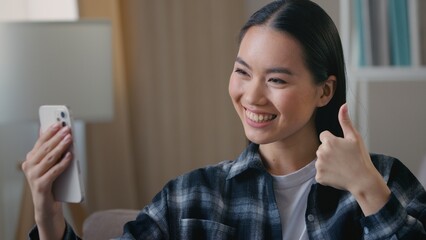 Smiling Asian Korean woman girl blogger talking video call waving hand mobile phone ethnic female vlogger greeting remote online chat conversation smartphone webcam distant communication app at home
