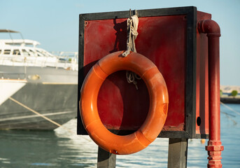 Lifebuoy and safety box at the marina with boats in the background during daylight hours