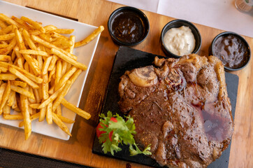Large plate of grilled beef steak with sides of fries and sauces served in a casual dining setting