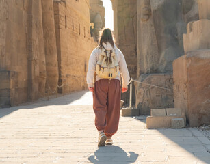 Person walking through ancient ruins in Luxor Temple with sunlight filtering down on a clear day