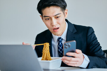 カップ焼きそばを食べながらスマホを操作する20代の若い男性