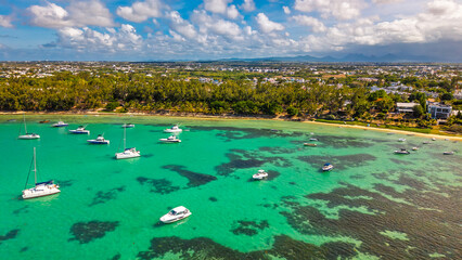 Stunning aerial view of a tropical turquoise lagoon with luxury yachts and catamarans anchored near a beautiful sandy beach and lush green coastline on a sunny day. © Yuliko