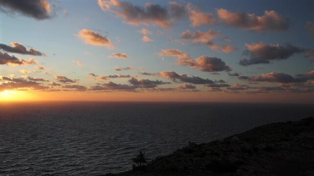 Dramatic sunset over the horizon of the Mediterranean Sea at Dingli Cliffs in Malta, with deep orange and red colors reflecting on the water under a dark cloudy sky. Sea sunset in Malta. 4k video