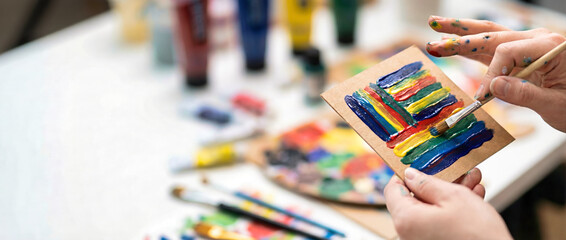 Close-up of artist hands painting colorful acrylic strokes on kraft paper. Creative art studio background with copy space. Painting workshop concept