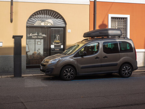 Gray Citroen Berlingo with roof box parked outside a violin maker's shop