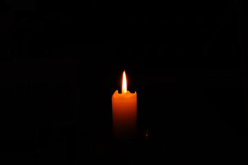 Single burning candle glowing in the dark. Atmospheric minimalist photography of a bright flame against a black background, symbolizing hope, spirituality, mourning, or peaceful silence