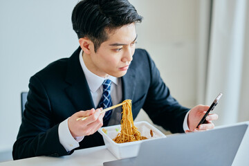 カップ焼きそばを食べながらスマホを操作する20代の若い男性
