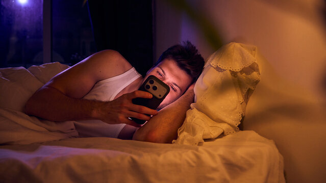 Man reading smartphone messages while lying on pillow. Concept of mobile communication, messaging apps, digital interaction, real time connectivity, smartphone technology, online services. - Powered by Adobe