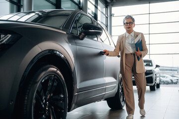 Businesswoman in stylish attire approaches modern SUV in a car dealership, showcasing professionalism and confidence in the automotive environment