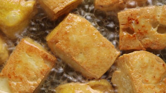 Yellow tofu frying in boiling oil. Top view shot