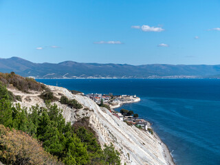 Panoramic view of the sea from a rocky hillside with pine trees under a clear blue summer sky