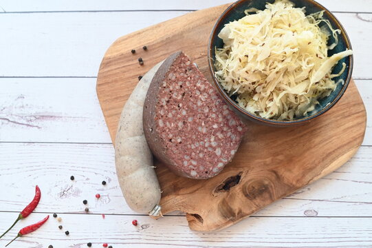 Top-down view of traditional Czech butcher products including blood sausages (jitrnice), pork offal sausages (jelita), and sauerkraut. Authentic Czech slaughterhouse cuisine presented in a rustic styl