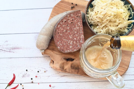 Traditional Czech food background featuring beer and classic slaughterhouse specialties such as blood sausages (jitrnice) and pork p&acirc;t&eacute; (prejt) arranged on a rustic wooden cutting board.