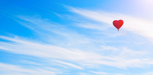 Fototapeta premium Red heart shaped balloon flying in the sweeping blue sky, romantic travel background, suitable for St Valentines day