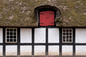 The house shows a red door at the top near a thatched roof. It has white walls with dark wooden beams. Windows are below the door. This scene is simple and rustic.
