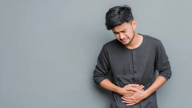 Health Crisis: A person struggles with discomfort, his face contorted in a grimace as he clutches his abdomen, likely indicating some form of stomach illness or pain.