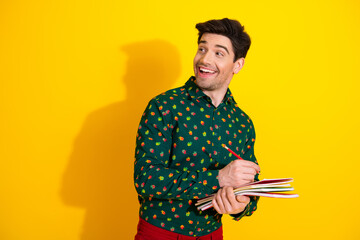 Happy young man in a green printed shirt smiles while writing in notebooks against a bright yellow background for lifestyle promotion and shopping themes