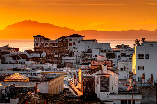 Picturesque view of the Moroccan coastline during orange sunrise with buildings on the shore seen from coastal surf town Tarifa in Spain.